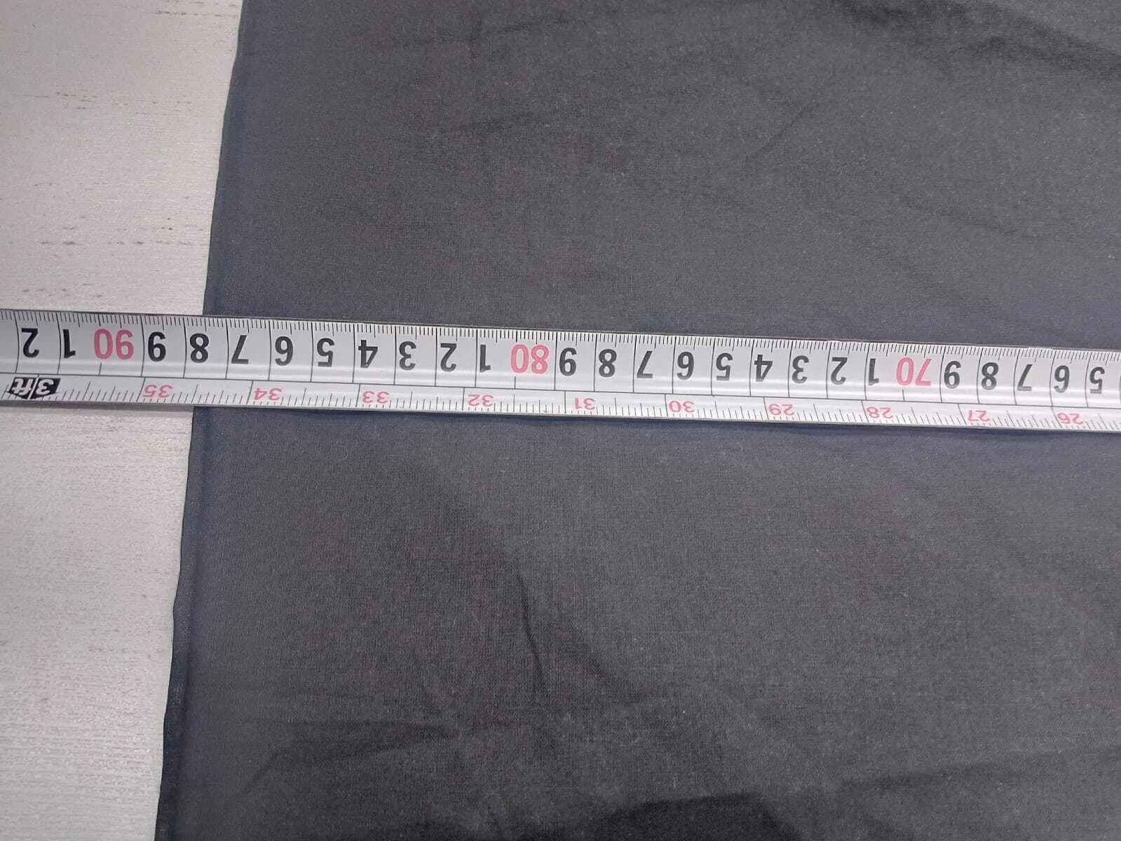 A steel tape measure laid across a width of dark grey cotton on a white inspection table.