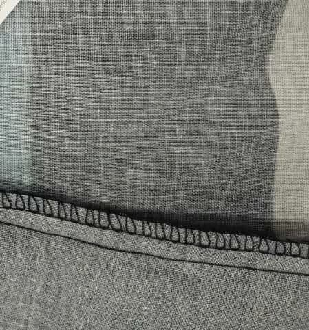 A close view of an overlocked seam running across grey woven cotton.
