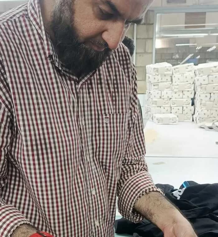 Humayun in a checked shirt on a factory floor, examining a finished garment over a work table.