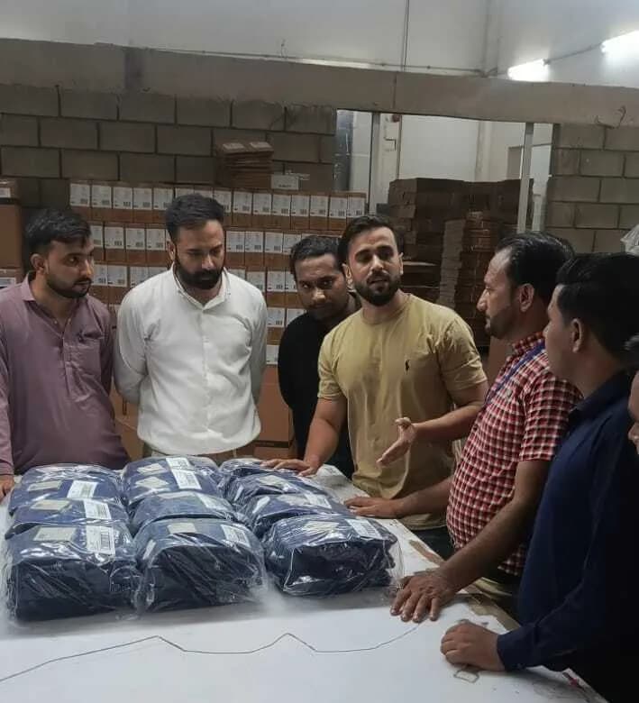 Several people standing around packed and bagged garments laid out on a white table in a packing store.